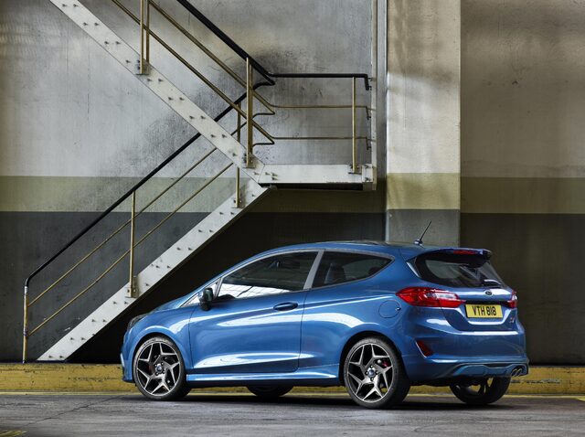 2018 Ford Fiesta ST blue hatchback rear three-quarter view against industrial staircase backdrop