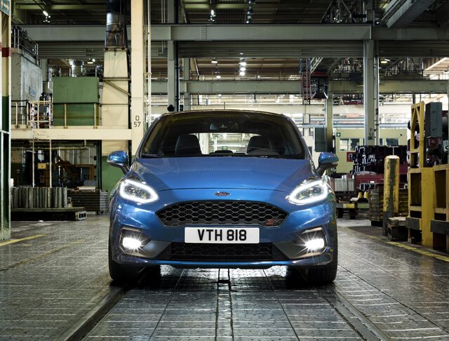 2018 Ford Fiesta ST blue hatchback straight-on front view inside industrial facility with headlights on