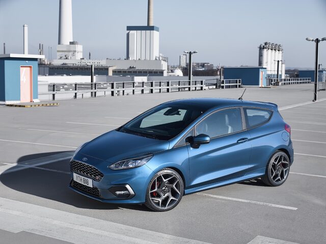 2018 Ford Fiesta ST blue hatchback front three-quarter view on open rooftop with industrial backdrop