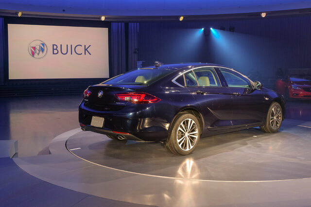 2018 Buick Regal Sportback blue rear three-quarter at reveal with Buick logo backdrop