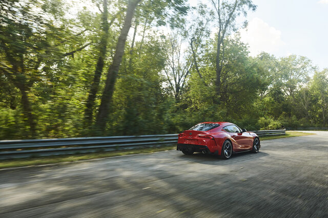 2020 Toyota GR Supra red rear three-quarter panning shot on sunny track road