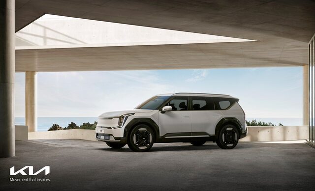 2024 Kia EV9 front three-quarter view in white, parked beneath a modern coastal architecture canopy with ocean views
