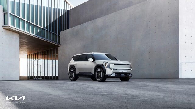 2024 Kia EV9 front three-quarter view in white against a modern urban concrete building facade