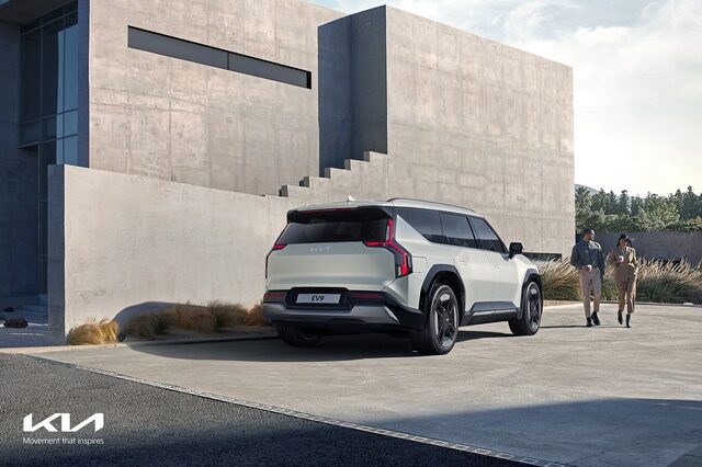 2024 Kia EV9 rear three-quarter view in white showing taillights and rear design, with two people walking nearby