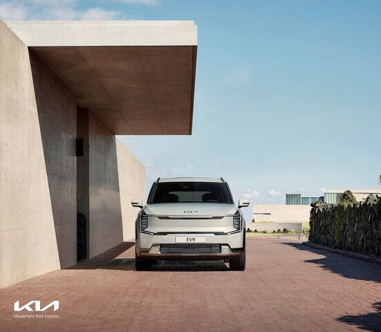 2024 Kia EV9 straight rear view in white, parked in a driveway, showing full-width taillights and rear fascia design