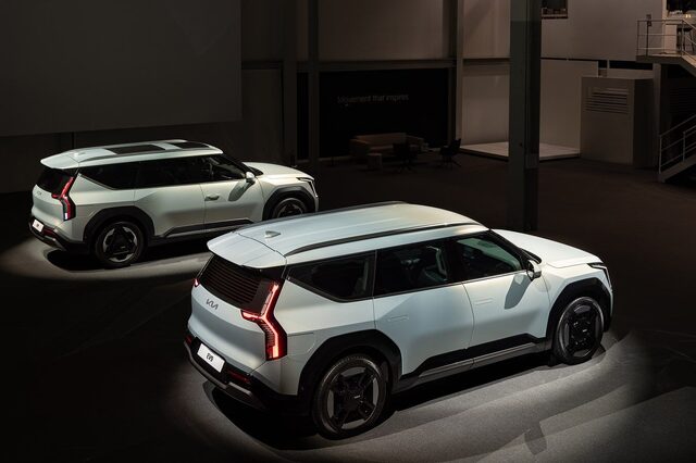 Two 2024 Kia EV9 SUVs on the global premiere reveal stage, rear three-quarter view showing taillights and roof design