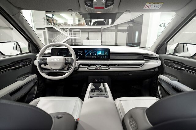 2024 Kia EV9 interior wide view showing the dual touchscreen dashboard, E-GMP flat floor, and light gray two-tone cabin