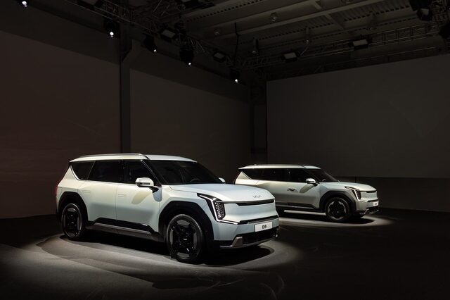 Two 2024 Kia EV9 electric SUVs on the global premiere reveal stage under dramatic spotlights, front three-quarter view