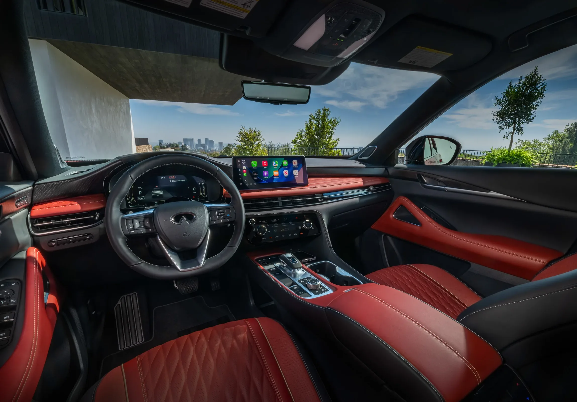 2027 Infiniti QX65 interior front cabin view showing red and black leather seats, dual displays, and panoramic roof