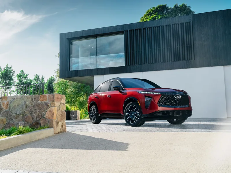 2027 Infiniti QX65 Sport Exterior Front Three-Quarter View Sunfire Red in Front of Modern Architecture