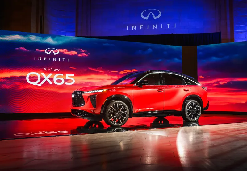 2027 Infiniti QX65 Sport World Reveal Press Event on Stage with All-New QX65 Signage Sunfire Red